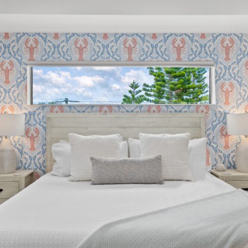 Drift into coastal comfort in this bright bedroom, featuring playful seaside wallpaper, soft linens, and a peaceful view of the Florida sky.
