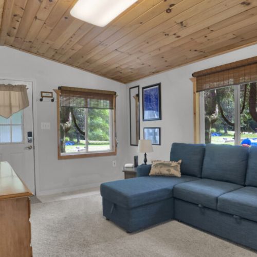 Comfortable lounge space with a sectional sofa, warm wood accents, and a serene view of trees through the windows.